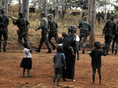 An unidentified woman and group of children watch as Colonial Portuguese soldiers train in the woods, Ancuabe, Cabo Delgado Province, Mozambique, July 27, 1973. The country gained its independence from Portugal during Mozambican War of Independence, which lasted from 1964 until 1974. (Photo by David Hume Kennerly/Getty Images)